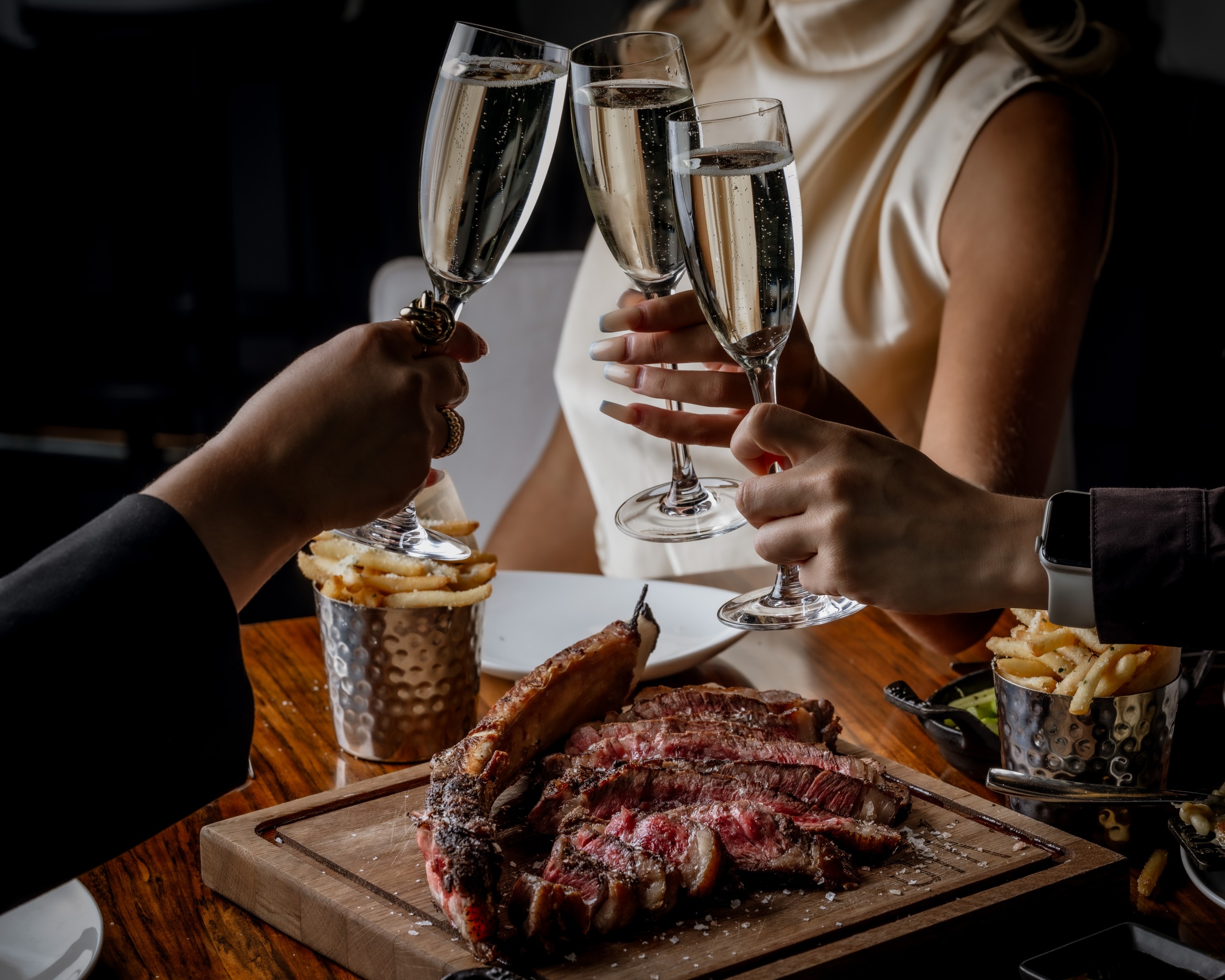 Cheers to STK. Happy diners enjoying a toast of Sparkling White Wine with steak and fries placed on the table