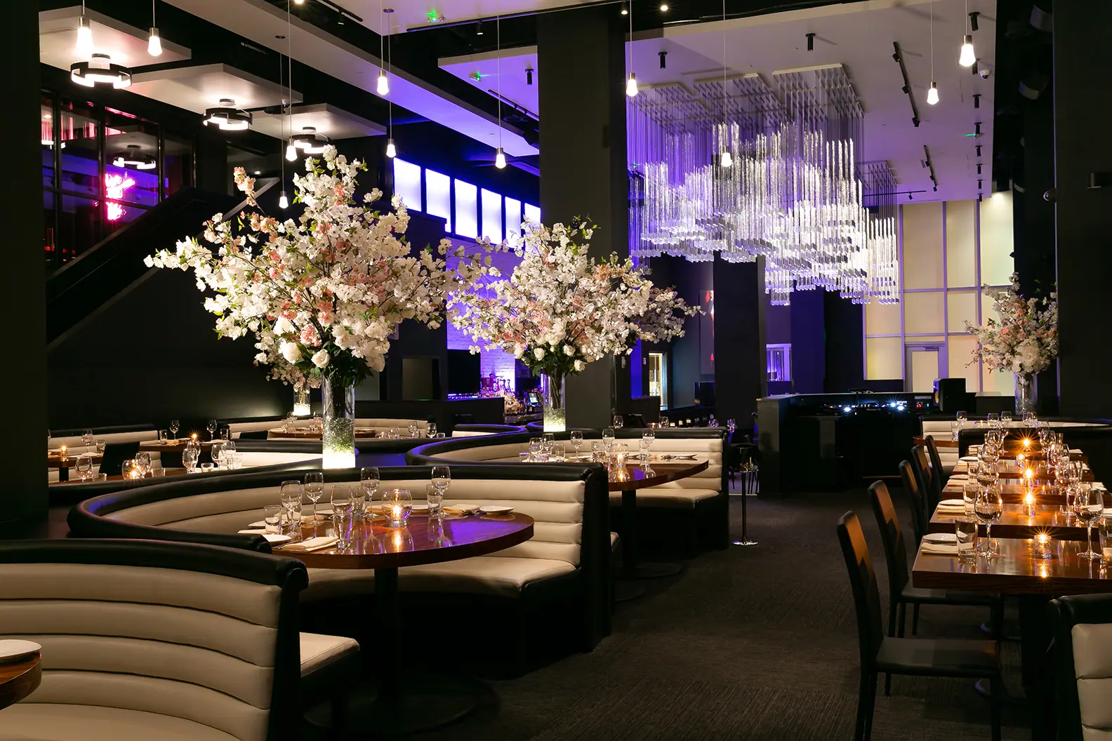 Interior shot showing curved banquette seating, large floral centerpieces on the tables and hanging glass chandeliers, softly lit