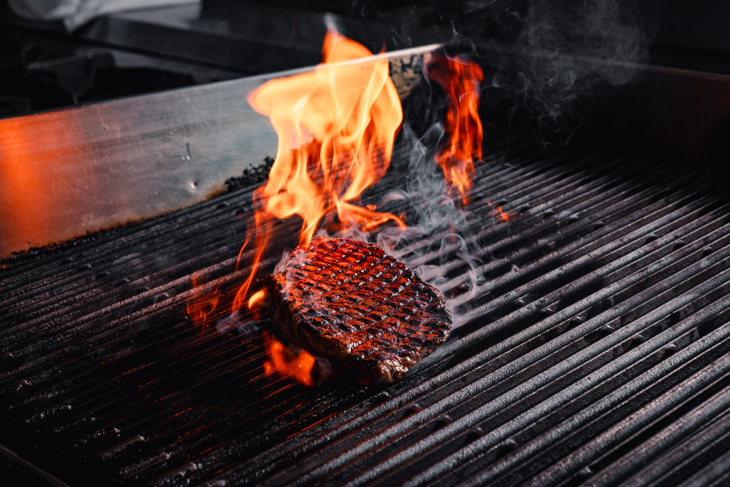 Flame grilled burger patty charring over open flames on a hot restaurant grill.