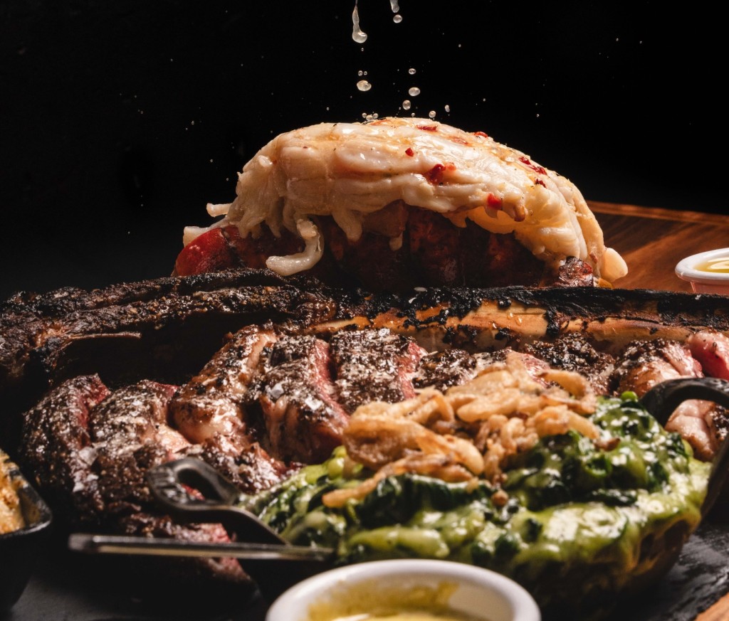 A beautifully delicious tomahawk steak with a juicy lobster that is getting lemon squeezed on it.