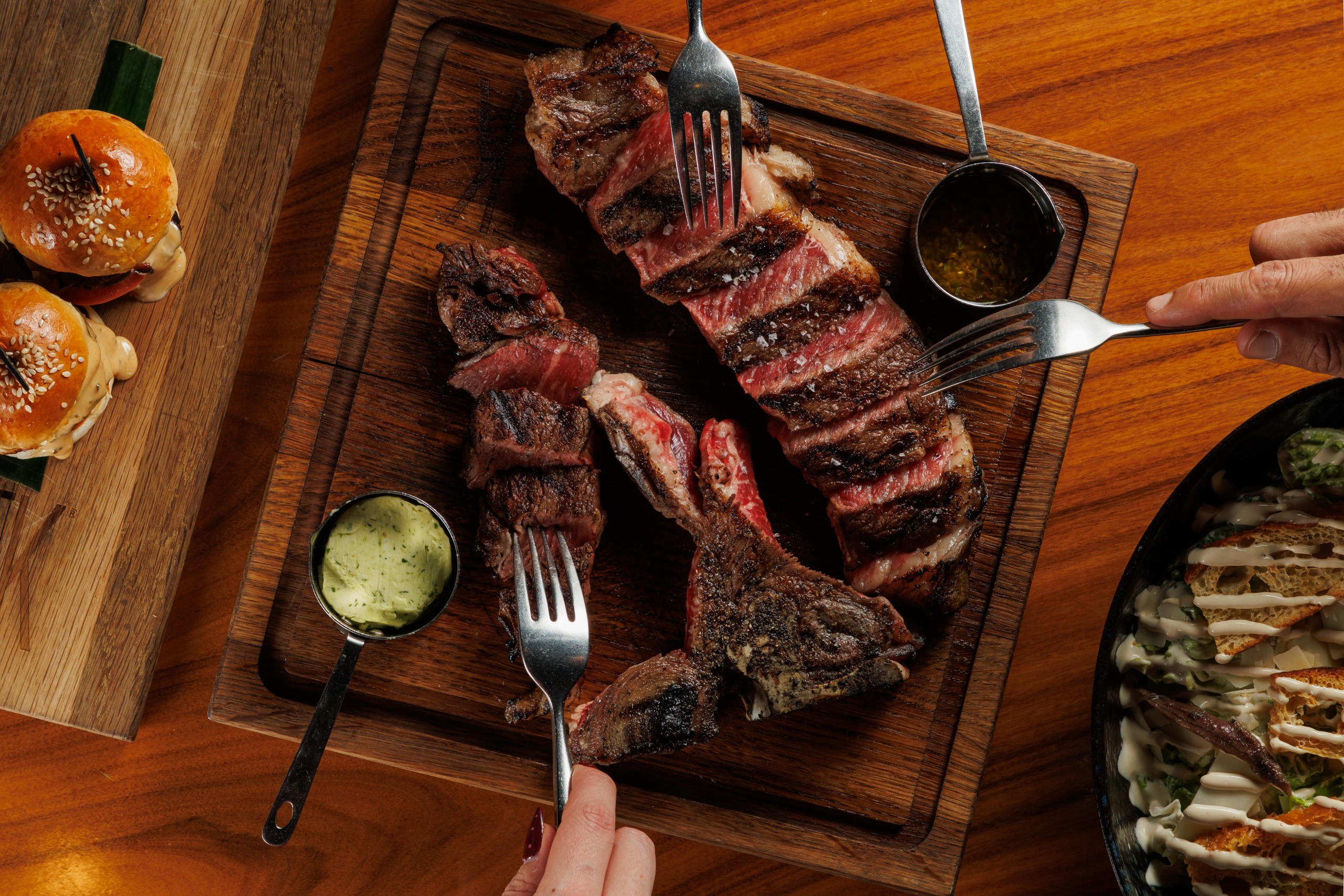 a group of people picking up slices of premium steak with forks
