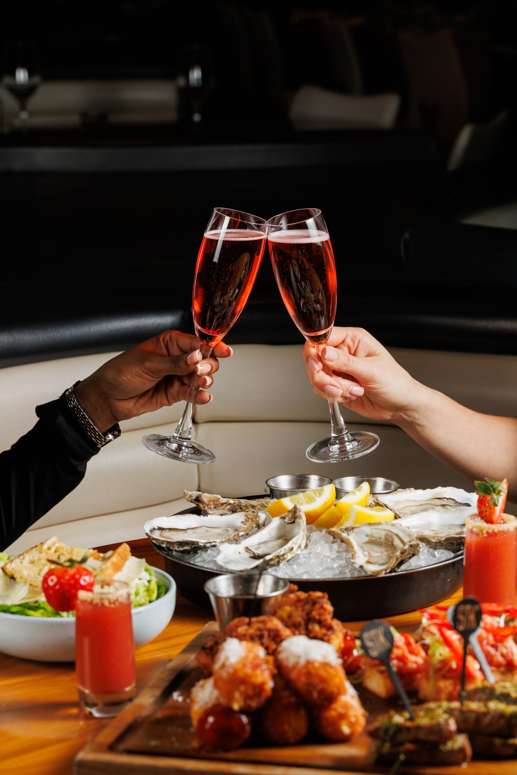 Two people clinking glasses with a table full of steak and seafood dishes